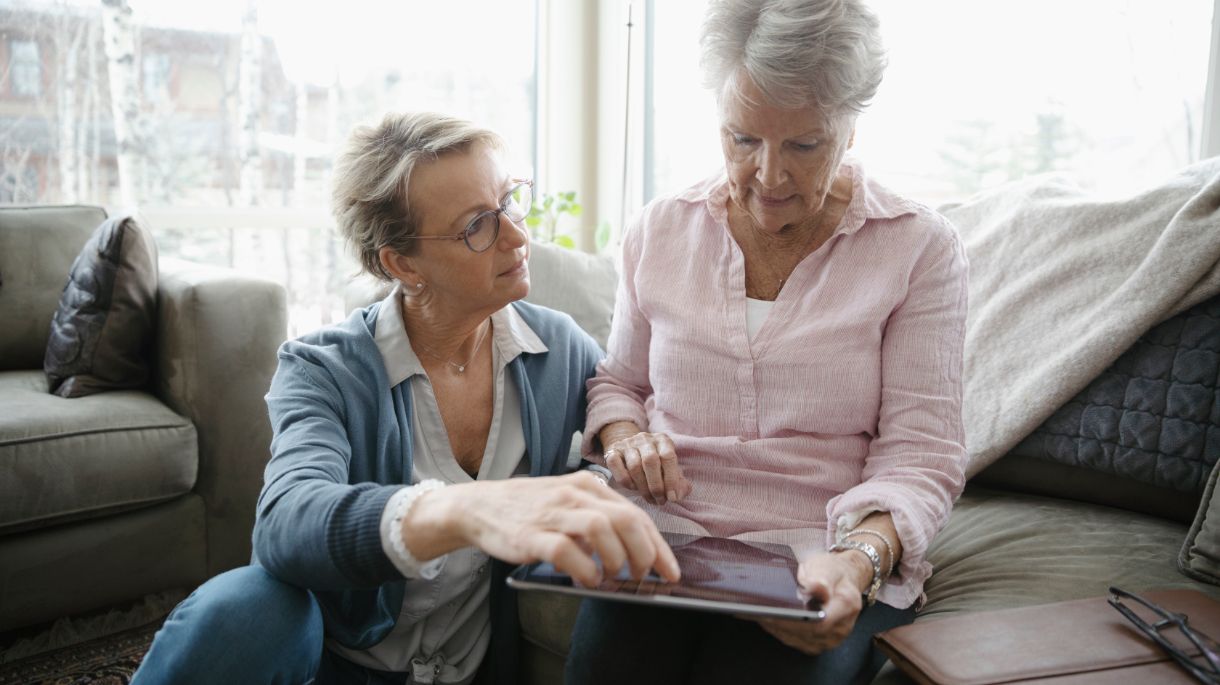 woman on couch using ipad with woman on floor helping