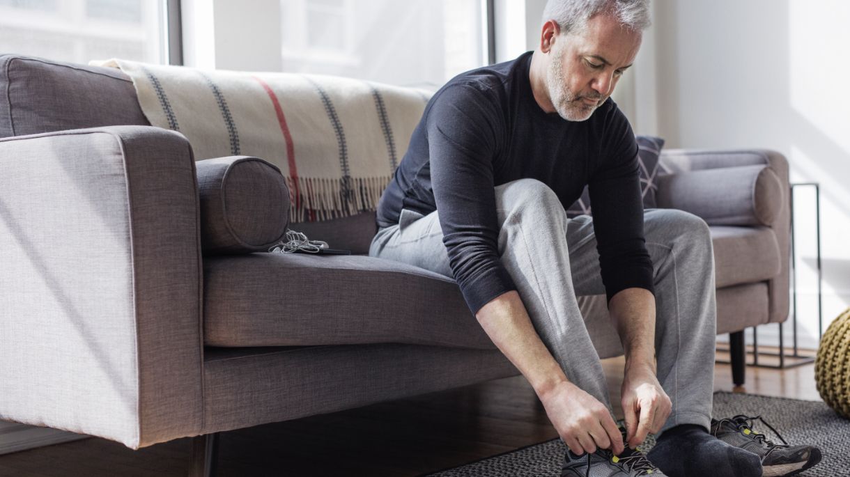 man putting on sneakers sitting on grey couch