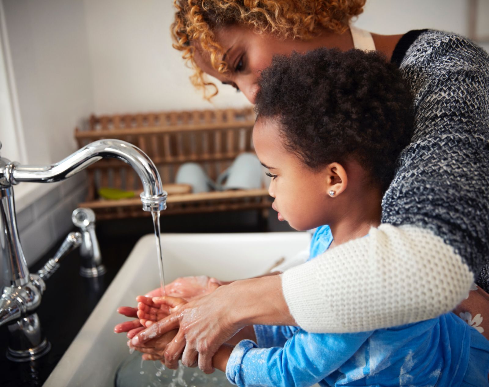 mother helping small child in blue shirt wash his hands at kitchen sink