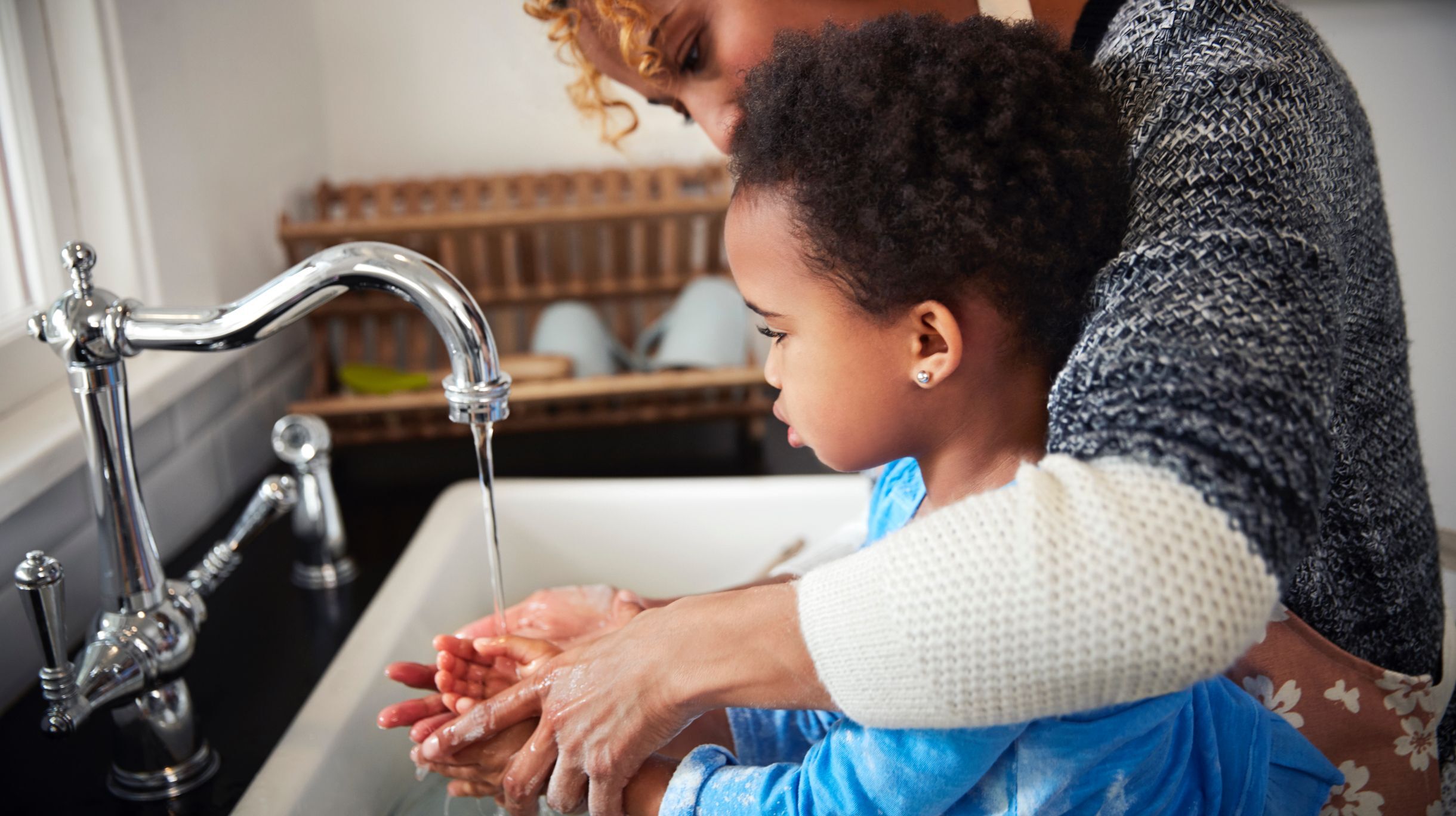 mother helping small child in blue shirt wash his hands at kitchen sink