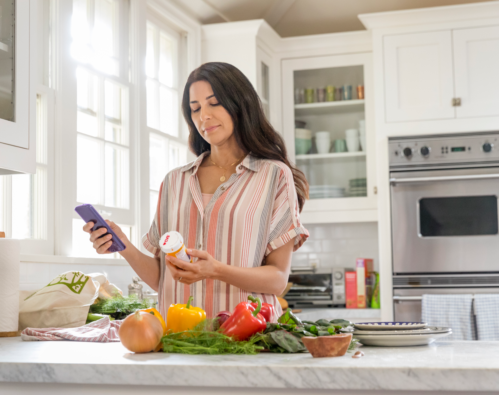 Caucasian woman in kitchen with veggies on the counter reviewing her cvs prescription on her phone