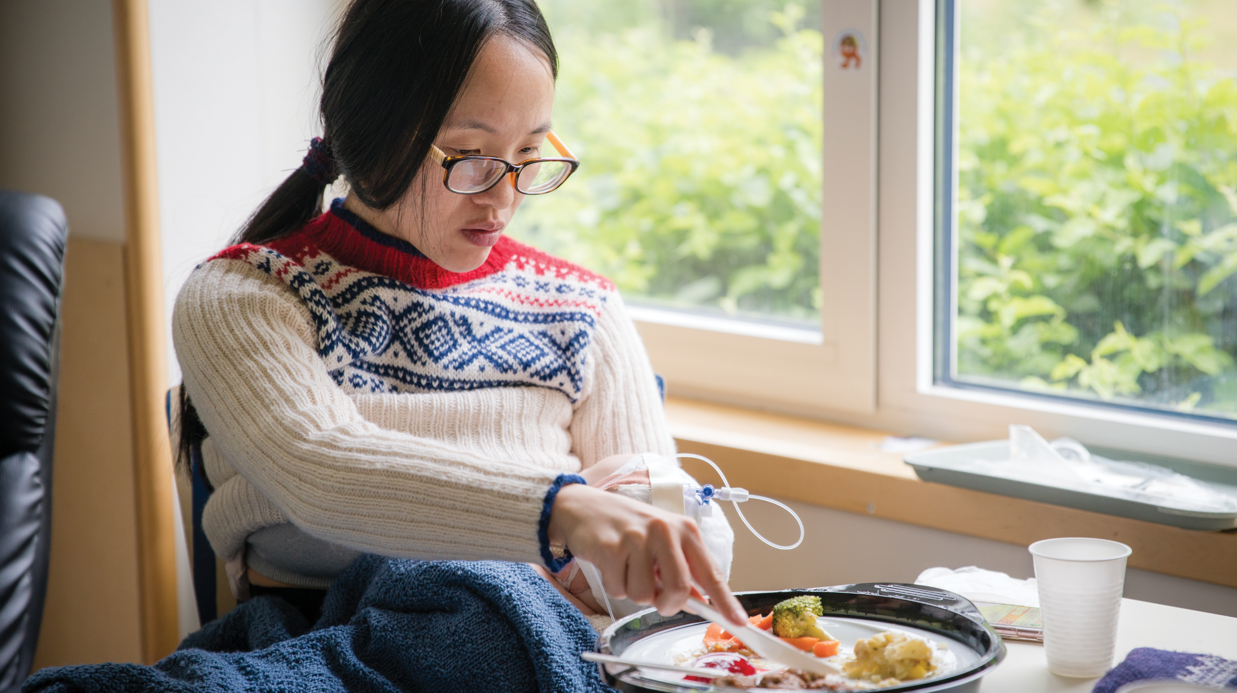 asian woman in glasses eating lunch while getting iv infusion at home