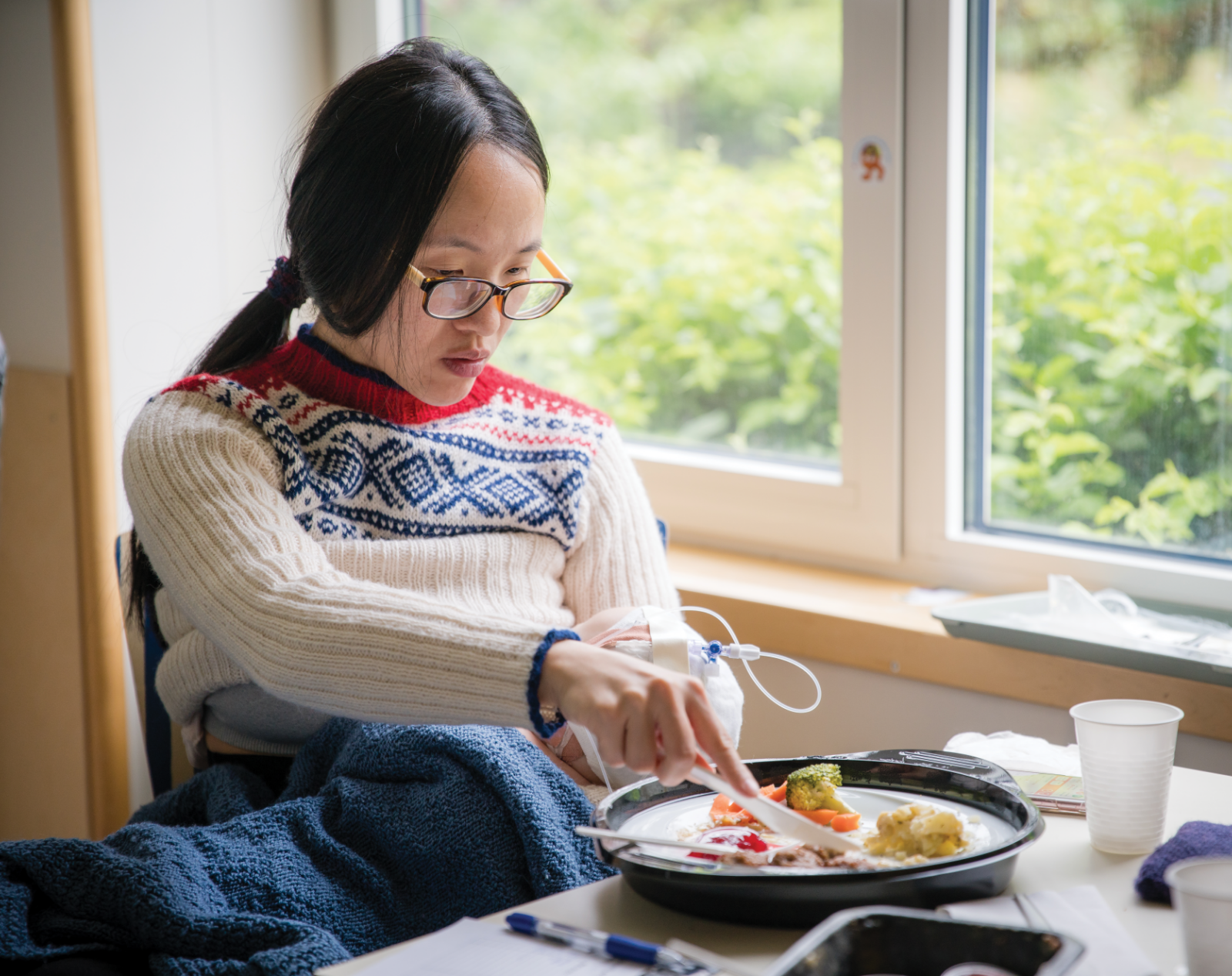 Asian woman in glasses eating lunch while getting iv infusion at home