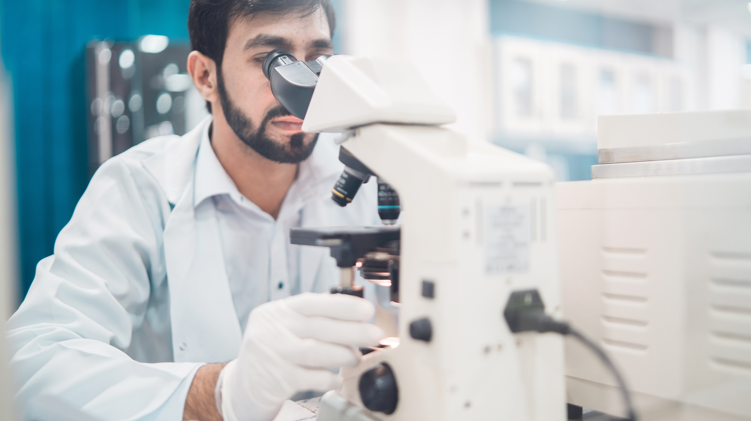 man in a lab looking through a microscope wearing gloves