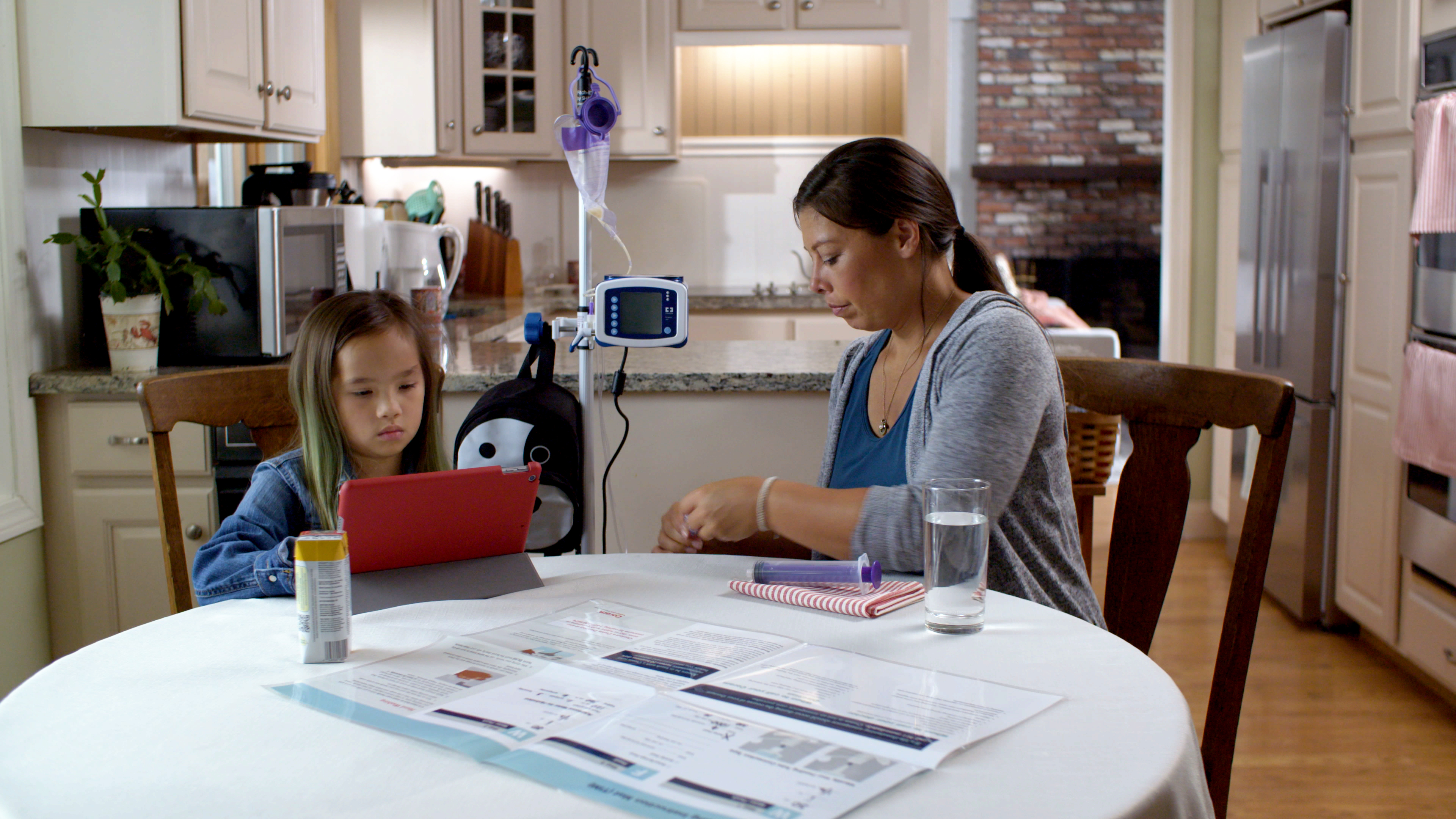 mother and daughter at kitchen table while daughter watches iPad while getting therapy