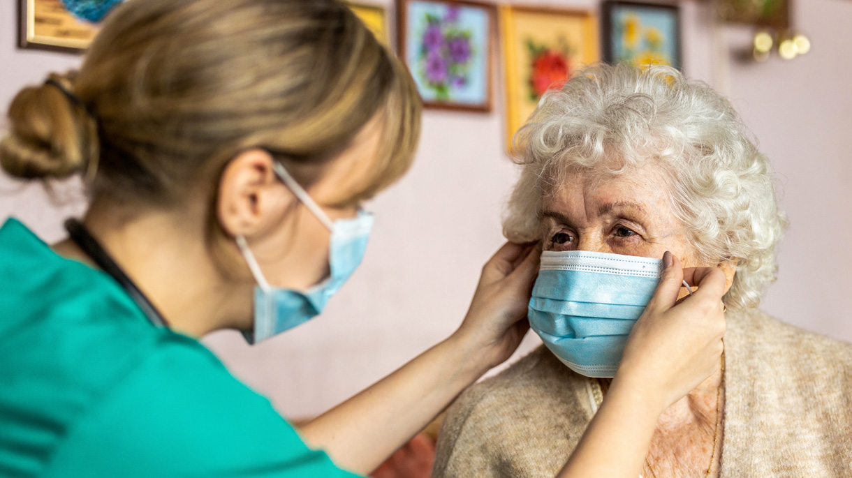 A masked nurse helping an elderly patient put on a mask
