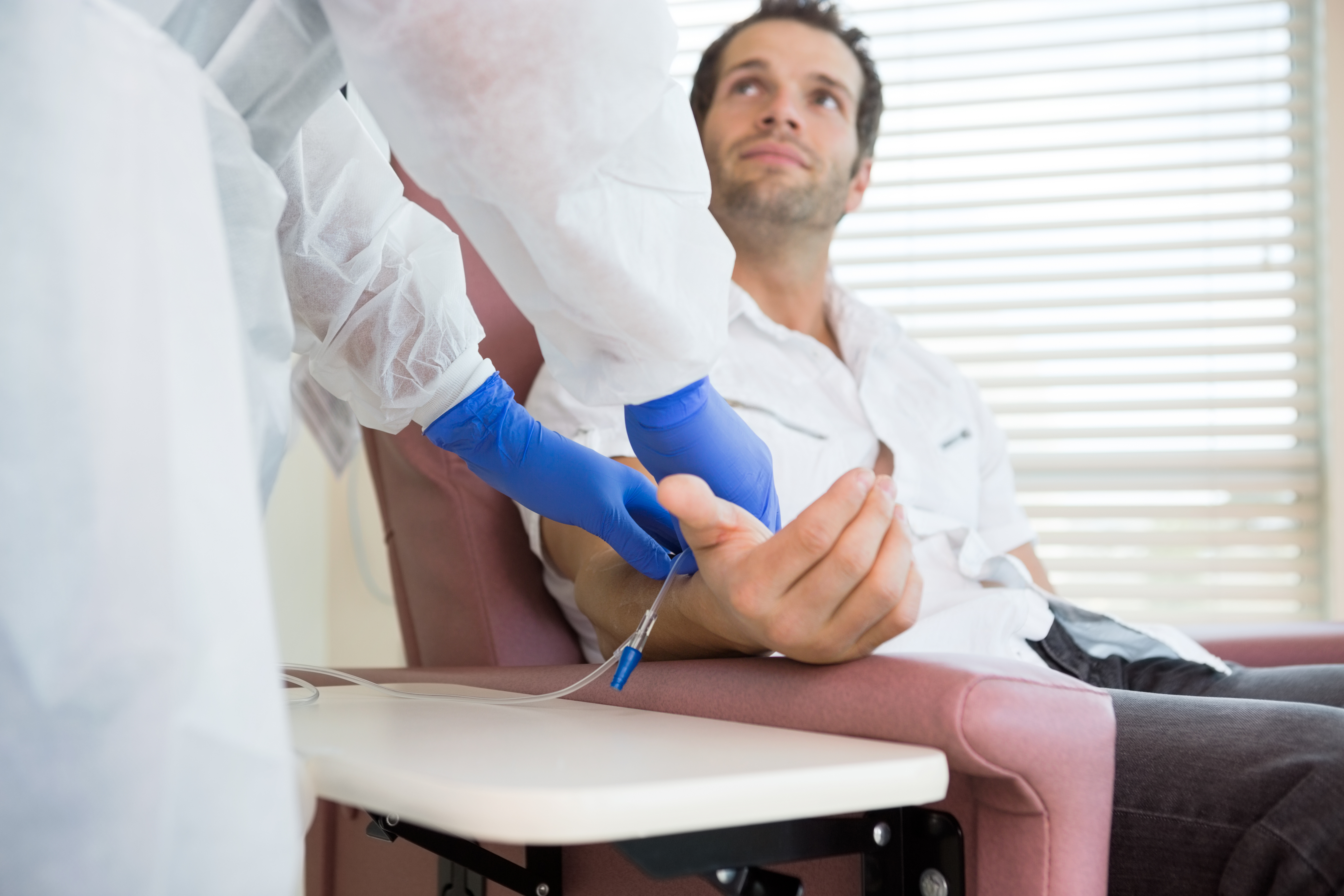 A man sitting in an infusion center chair looking up at his nurse 